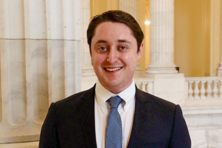 Man in black suit, blue tie, and white under shirt smiles for a headshot.