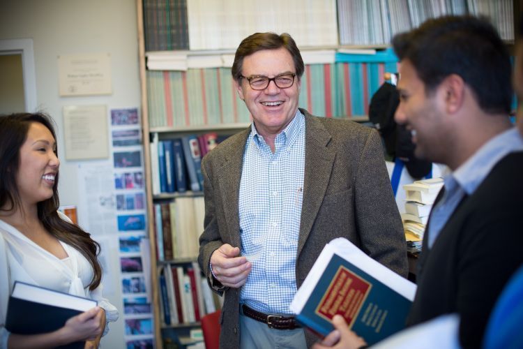 A professor laughs in his office with a few students