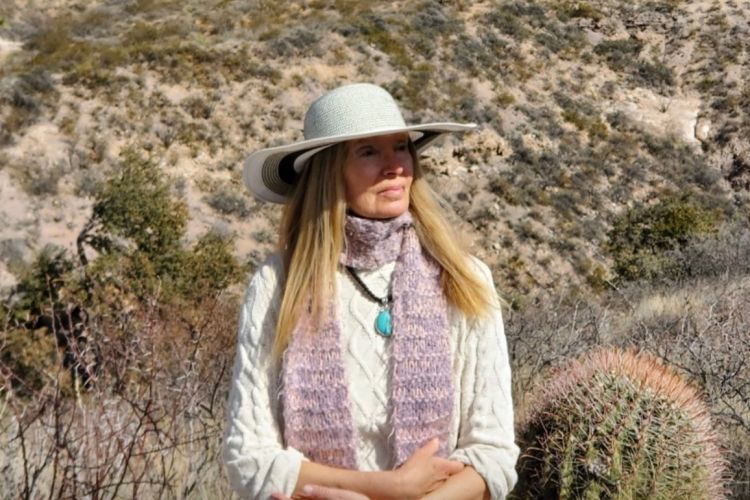 A woman sits on a rock outside and gazes off camera.