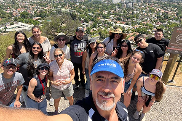 A group of students pose on a mountain top with the city below