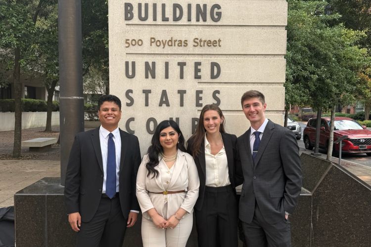 Four law students pose for a photo outdoors by a large sign