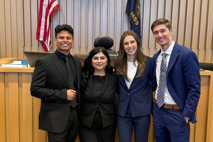 Four law students pose for a photo in a courtroom
