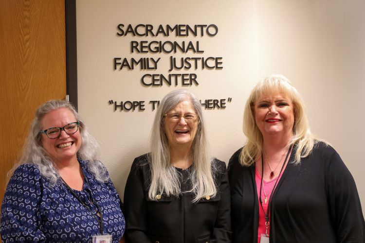 Three women stand in front of a sign that says "Sacramento Regional Family Justice Center." 