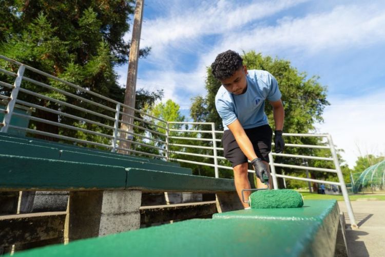 A student adds a coat of fresh green paint to a bench 