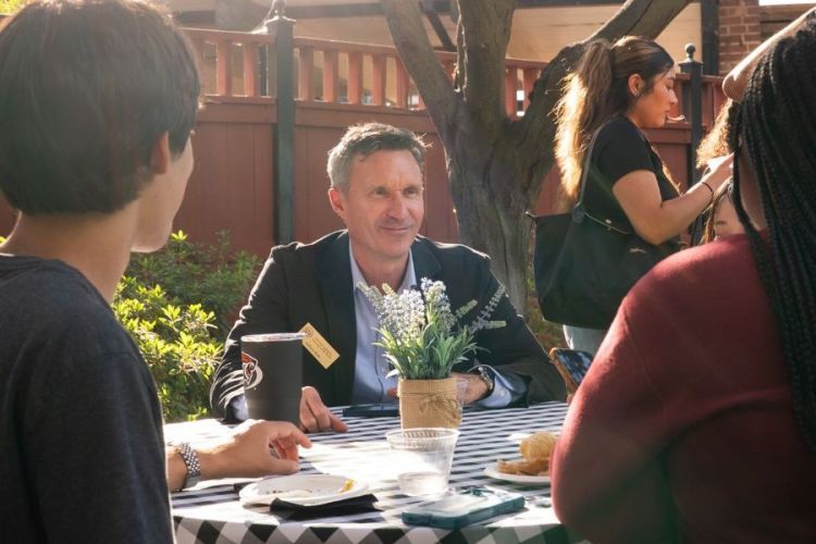 Professor Jeff Hole sits at a table outside with two students 