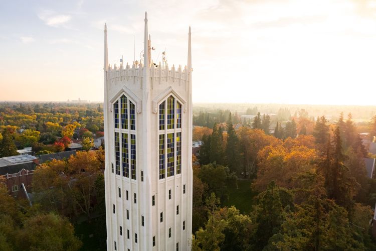 An aerial image of a tall white tower in front of fall foliage