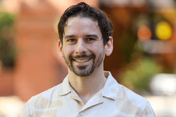 A man in a light colored button-up shirt smiles for a photo. 