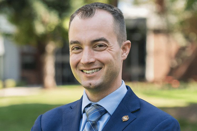 A man in a blue suit smiles for a professional photo. 