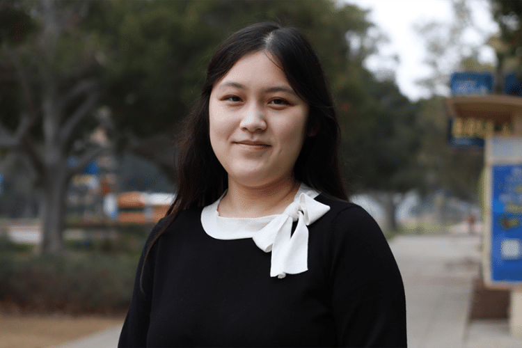 A woman with long black hair and black top smiles for a photo. 