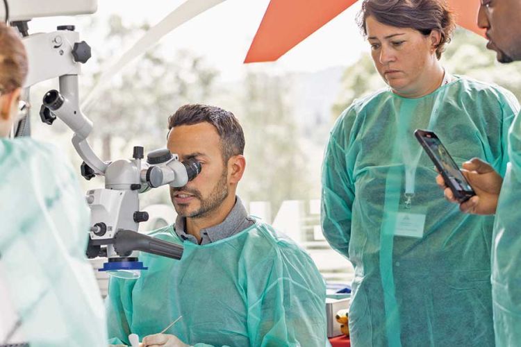 male doctor looking into microscope with person behind him