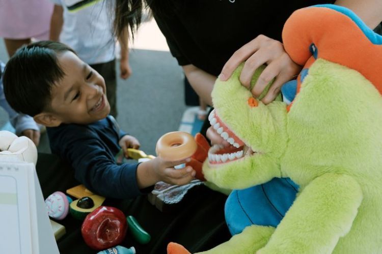 child placing a plastic donut into mouth of stuffed toy dinosaur