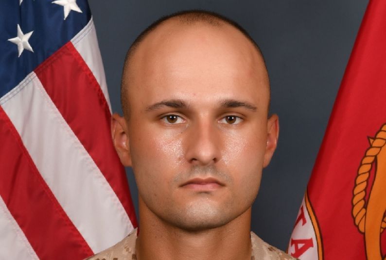 A portrait of Ian Worrell, wearing a military uniform. The background of the image is an American flag and another red flag.