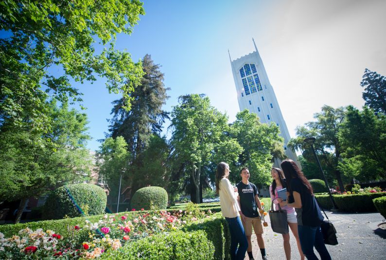 Four students stand in front of Burns Tower