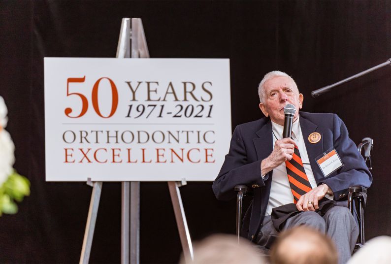 Richard Rutter sits in a chair next to a sign that reads 50 years of orthodontic excellence 