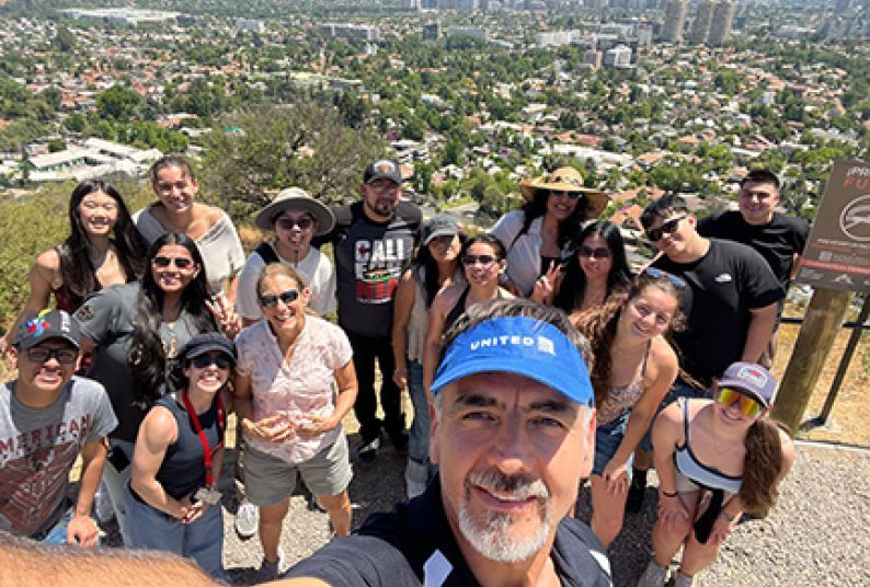 A group of students pose on a mountain top with the city below