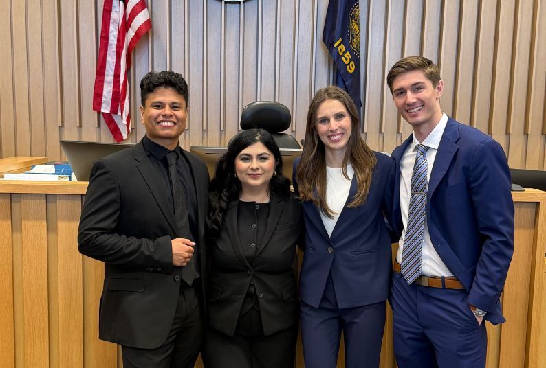 Four law students pose for a photo in a courtroom