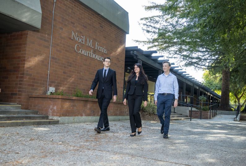 Three people in business attire walking in outdoor setting. 