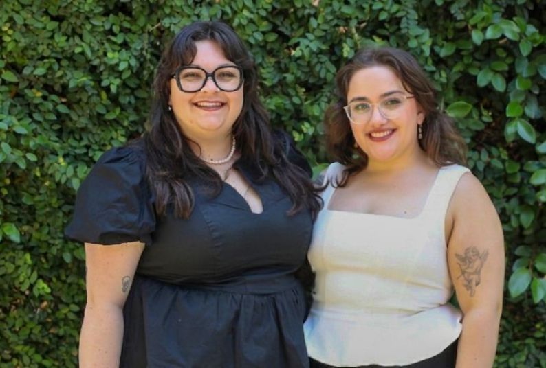 Two people stand against a green background for a professional photo. 