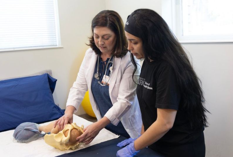 A professor showing a students a midwifery technique with a model 