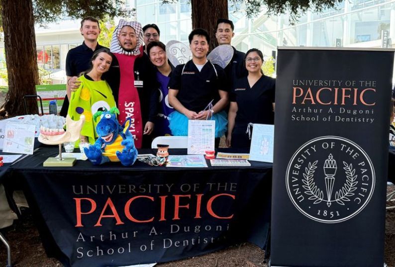 Eight people at a table outside with University of the Pacific, Arthur A. Dugoni School of Dentistry banner