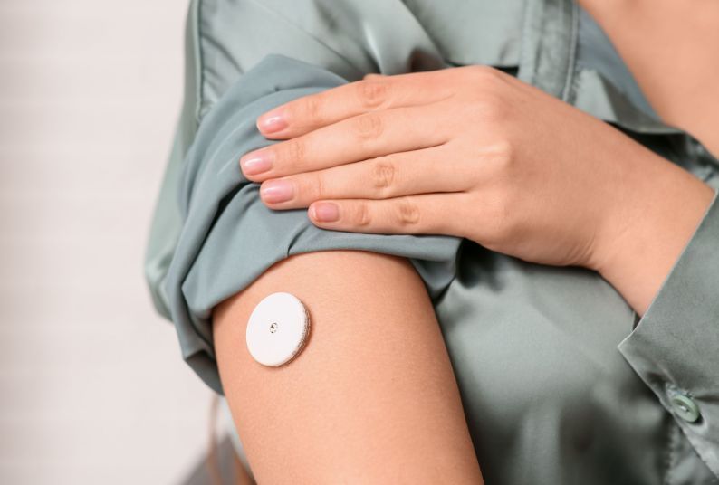 Photo of a person wearing a continuous glucose monitor on their right arm