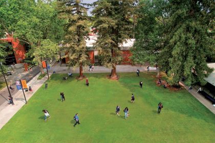 An aerial view of the Sacramento campus quad. Approximately 20 students are pictured in various locations on the quad. Lots of greenery and trees are visible. 