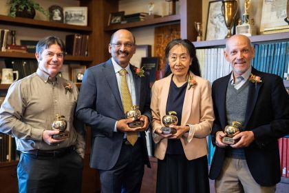 Four professors stand next to each other holding awards