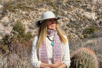 A woman sits on a rock outside and gazes off camera.