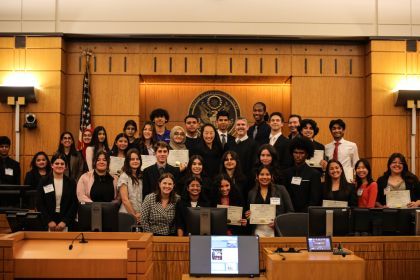 A group of high school students pose for a photo in a courtroom with a few judges