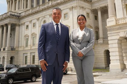 Two people wearing suits pose for a photo in Washington, DC