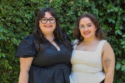 Two people stand against a green background for a professional photo. 