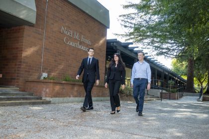 Three people in business attire walking in outdoor setting. 