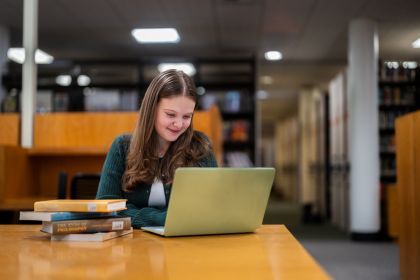 a student sits at a table looking at a laptop.