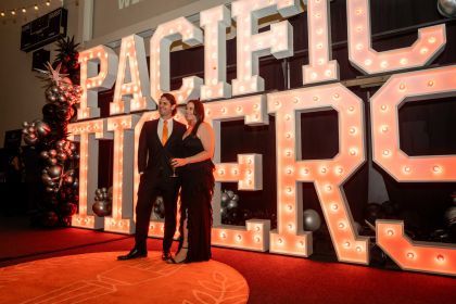 Two people dressed in black in from of a Pacific Tigers sign.