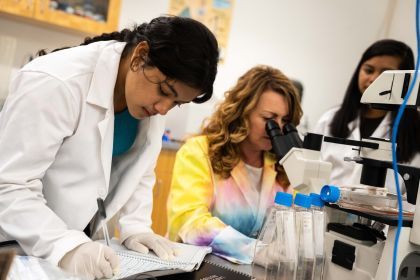 A student in a white lab coat writes in a notebook