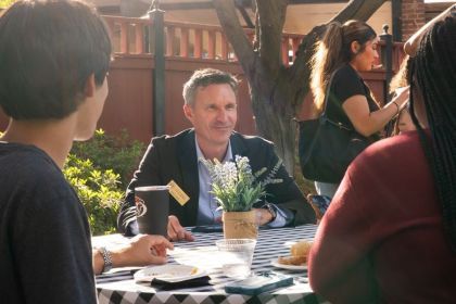 Professor Jeff Hole sits at a table outside with two students 