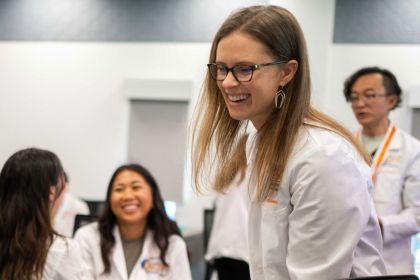 A faculty member in a lab coat smiling in the foreground