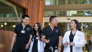 Photo shows four Nursing students at Pacific's School of Health Sciences talking and smiling while walking out of the nursing classroom.