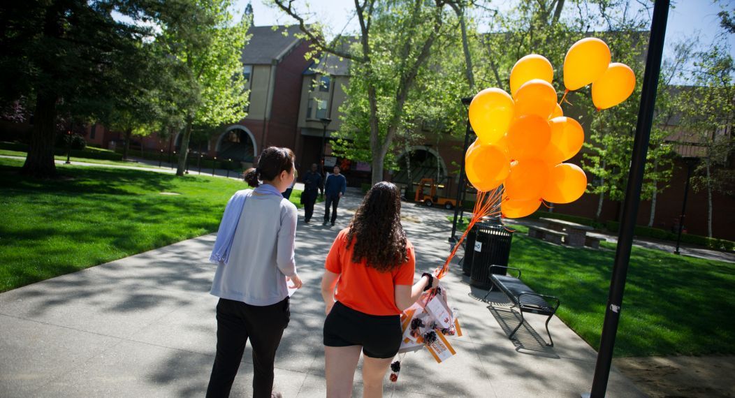two students walking with orange balloons
