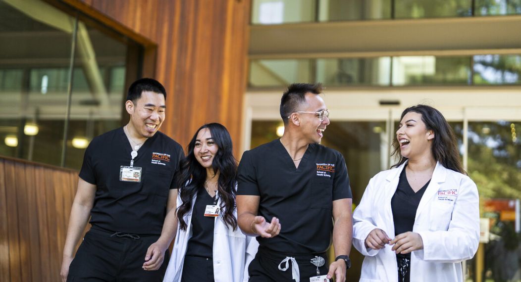 Photo shows four Nursing students at Pacific's School of Health Sciences talking and smiling while walking out of the nursing classroom.