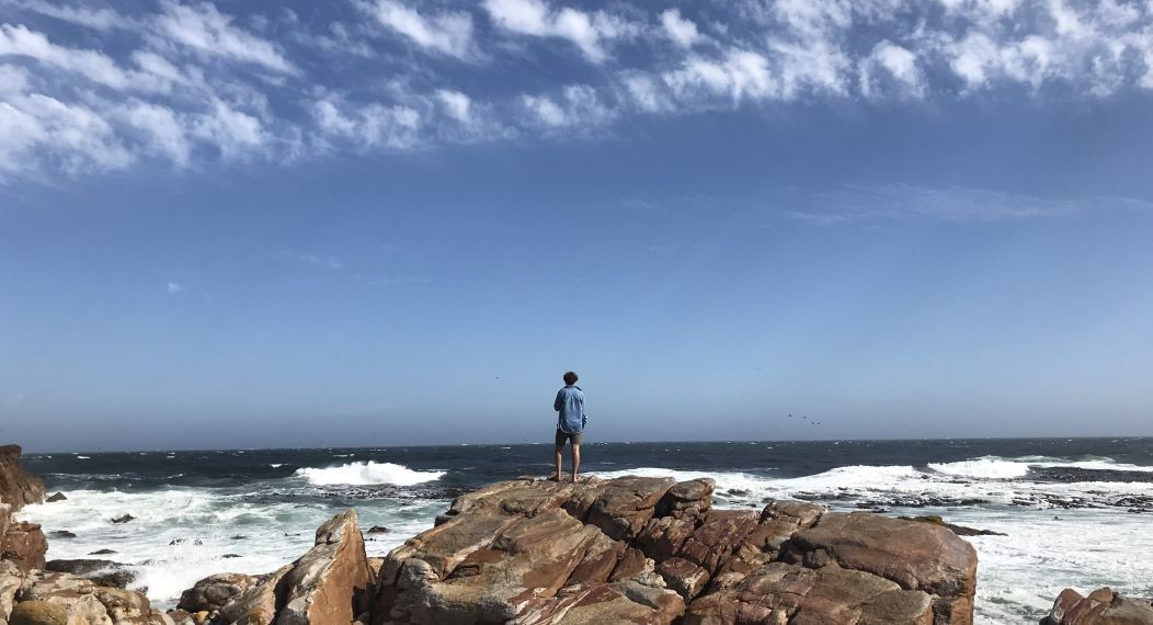 a student stands on rocks looking at waves