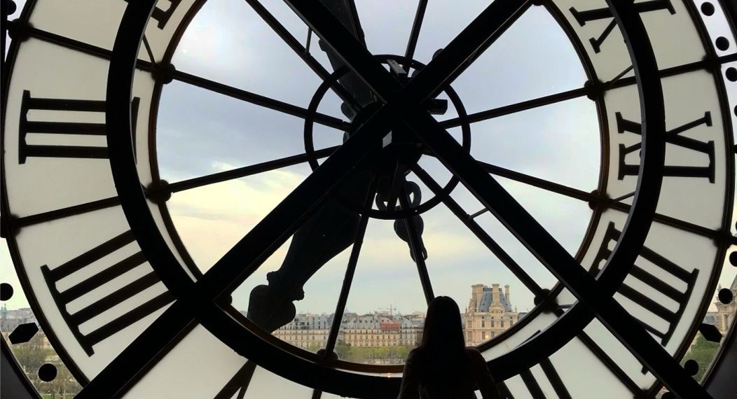 student stands behind clockface looking at european buildings