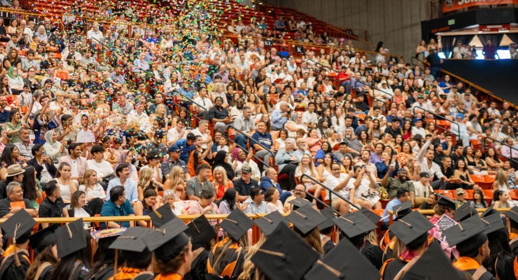 Confetti floats in the air above the bleachers full of guests watching Commencement