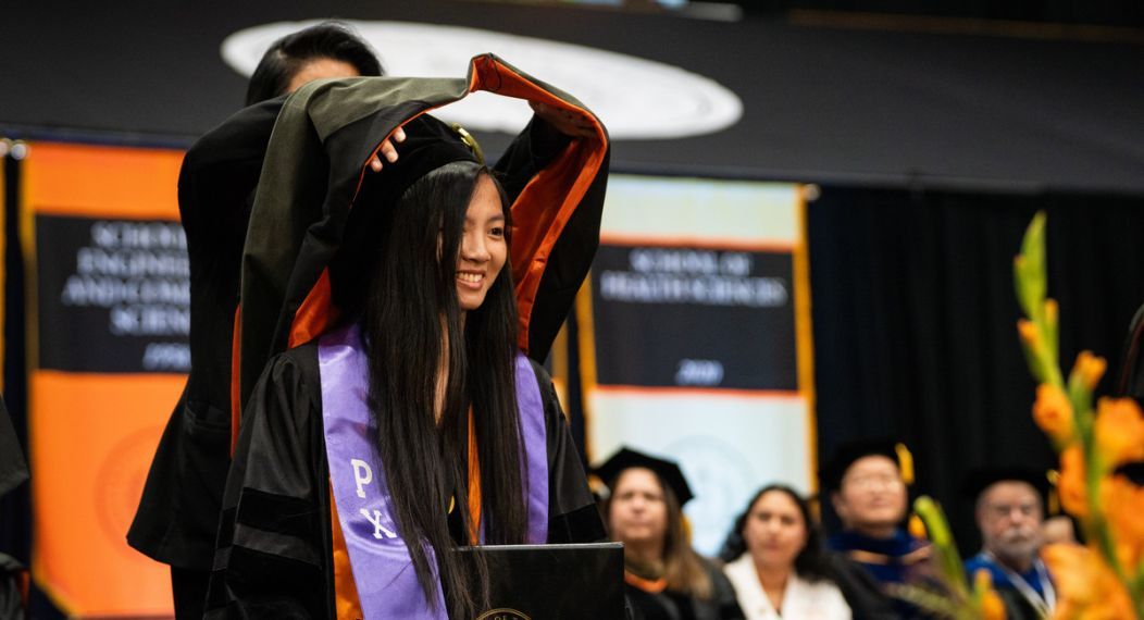 a pacific graduate receives her hood at commencement