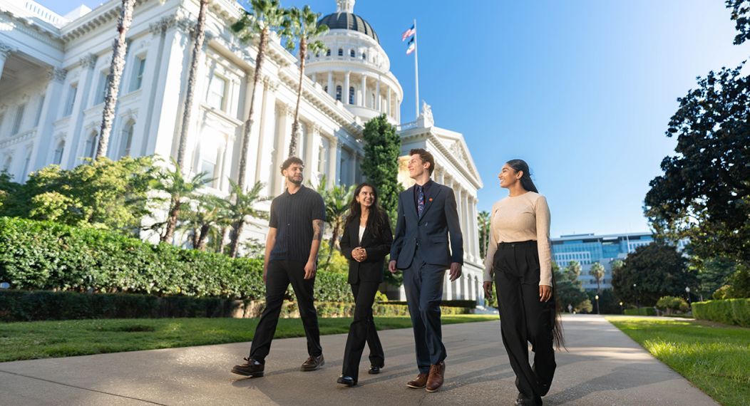 Image of 4 individuals walking in front of the Sacramento Capital Building. 