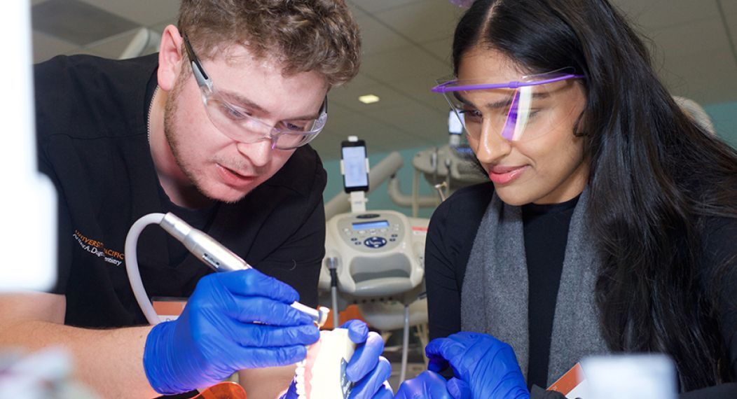male student guiding female attendee while holding a drill and typodont