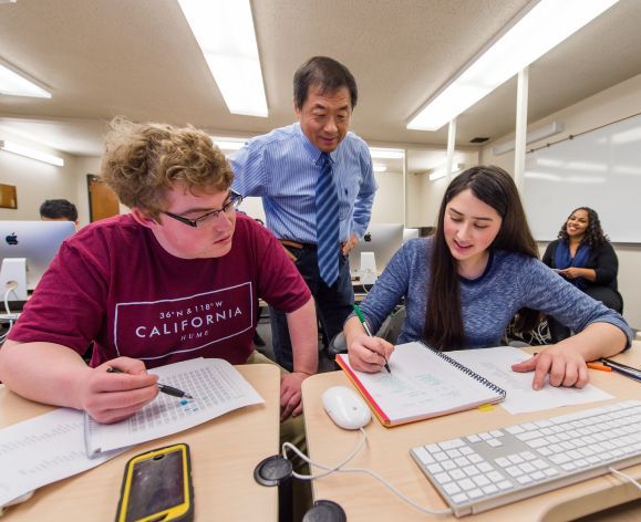 Male and female student working at a table with a faculty member helping