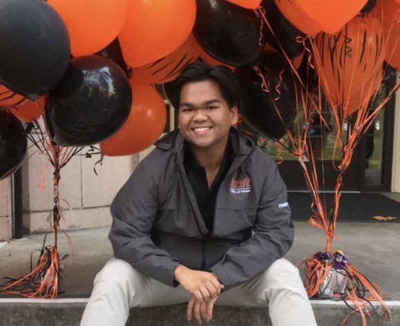 male student sitting on steps surrounded by orange and black balloons