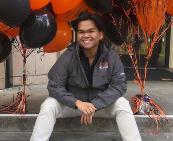 male student sitting on steps surrounded by orange and black balloons