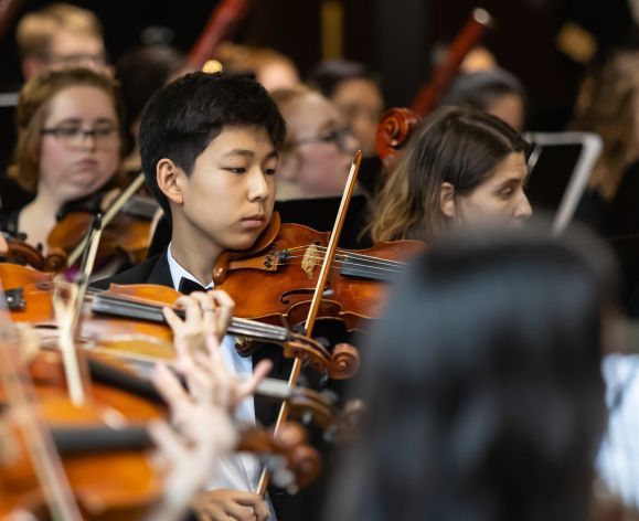 Young Student playing violin as part of orchestra